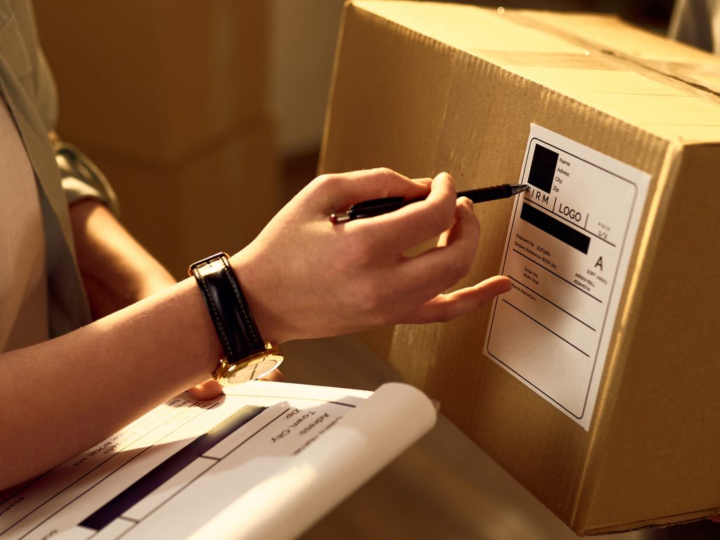 Two delivery women cooperating while checking data on the packages in the office.